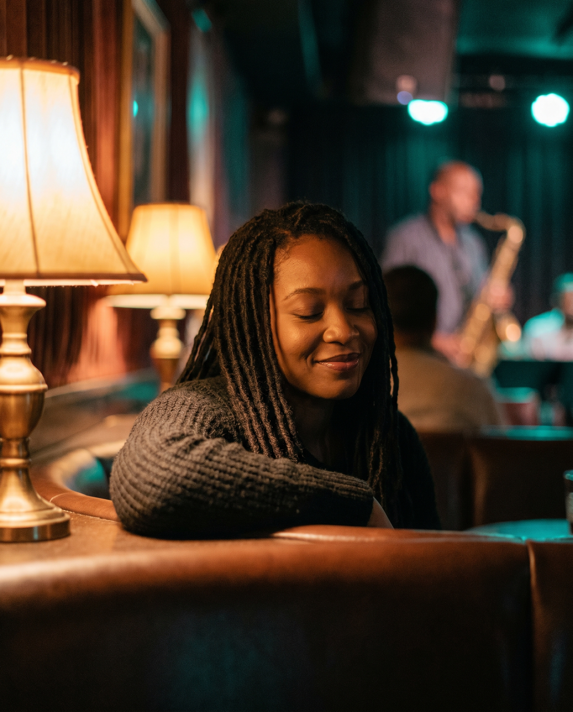 A Black woman with locs, eyes closed, listening in warm lounge light